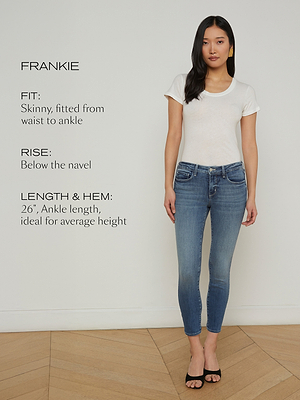 A woman stands indoors wearing a white t-shirt, blue ankle-length skinny jeans, and black sandals. Text beside her describes the jeans’ fit, rise below the navel, and ankle-length hem ideal for average height.
