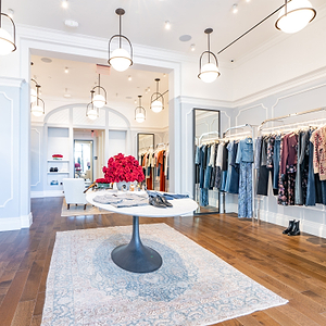 Modern clothing store interior with racks of clothes, a table with flowers, and chairs.