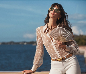 Woman holding a fan by a waterfront with a clear blue sky