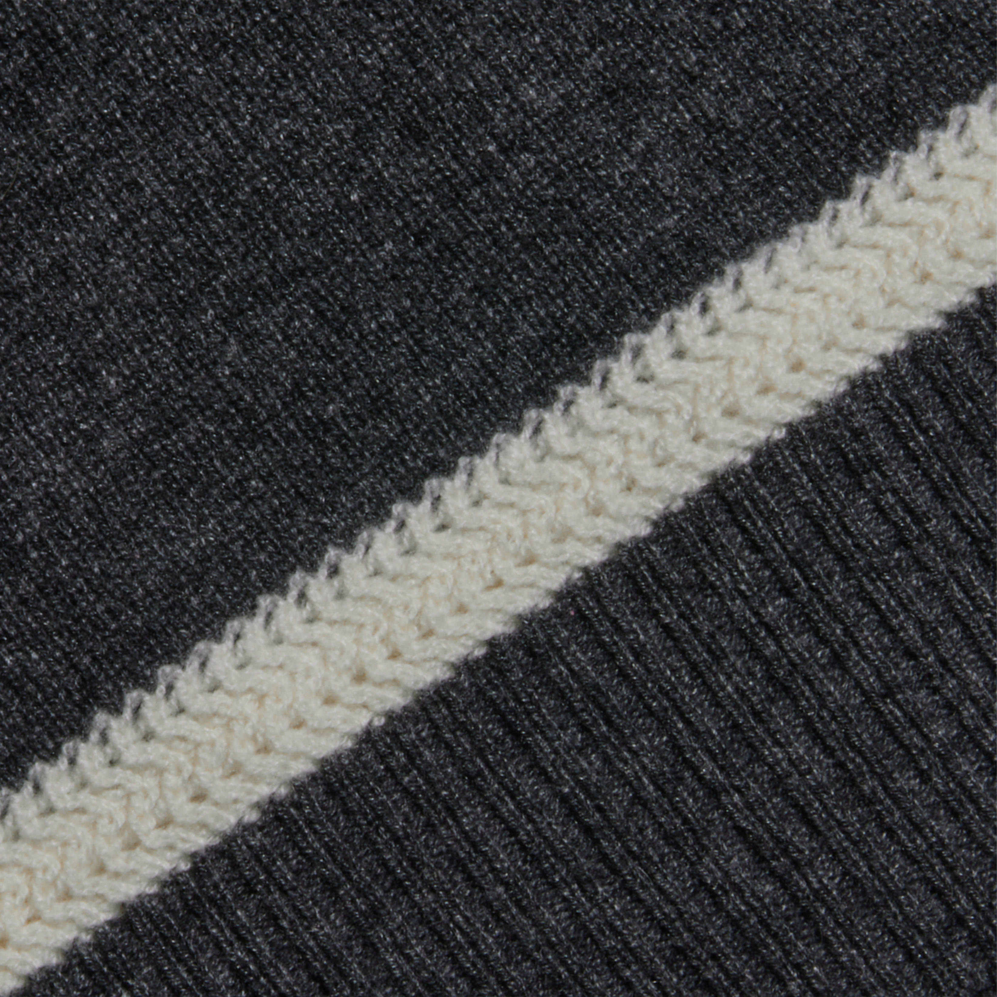 Close-up of dark gray fabric with a diagonal off-white knitted stripe running across it, showcasing the detailed texture and precise stitching.