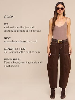 Woman in sunglasses and taupe tank top models brown barrel-leg jeans with patch pockets, dart and seam details. Text describes fit, rise, cropped length, and unique pocket features. Neutral background.