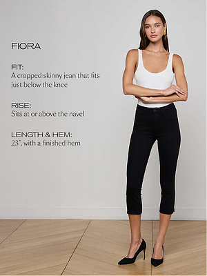 A woman wearing a white tank top and black cropped skinny jeans stands indoors on a wood floor. Text describes the jeans fit, rise, and hem length, with her arms relaxed by her sides.
