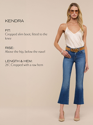 A woman wearing sunglasses, a cream camisole, a brown belt, and cropped blue jeans with a raw hem stands against a beige background. Text on the left describes the jeans’ fit, rise, and length.