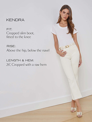 A woman stands against a white wall wearing a white t-shirt and the Kendra Cropped Flare Jean in vintage-white premium stretch denim, featuring a 26 raw hem and slim boot fit. She completes the look with beige heels and gold earrings.