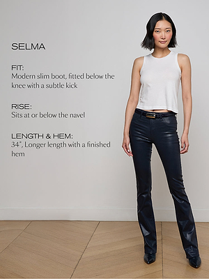 A woman stands indoors wearing a white sleeveless top and dark slim-fit bootcut jeans. Text on the left describes the jeans’ fit, rise, and length. She is smiling slightly with one hand in her pocket on a wooden floor.