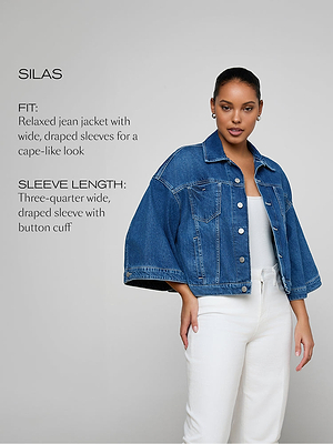 A woman wearing a blue denim jacket with wide, draped three-quarter sleeves over a white top and pants stands against a plain gray background. Text describes the jackets relaxed fit and cape-like sleeve style.