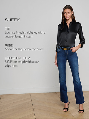 A woman stands indoors wearing a black satin blouse and dark blue straight-leg jeans. Text on the image describes the jeans’ fit, rise, length, and hem. The background features a light wall and wooden floor.