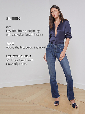 A woman stands in a room wearing a navy satin blouse and blue straight-leg jeans. Text describes the jeans’ fit as low-rise, straight, floor-length with a raw edge hem, and inseam of 32 inches.