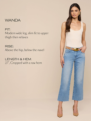 Eine Frau modelliert eine hellblaue, weit geschnittene Jeans mit offenem Saum, einem beigen Tanktop und hellbraunen Absätzen. Der Text beschreibt die Passform der Jeans: modernes weites Bein, schlank bis zum Oberschenkel, dann entspannt; Bundhöhe: oberhalb der Hüfte, unterhalb des Bauchnabels; Länge: 27-Zoll-Cropped.