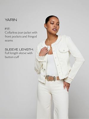 A woman wears a white, collarless jean jacket with front pockets, fringe seams, and button cuffs over a white top. She stands against a gray background. Text describes the jacket’s fit, sleeve length, and design details.