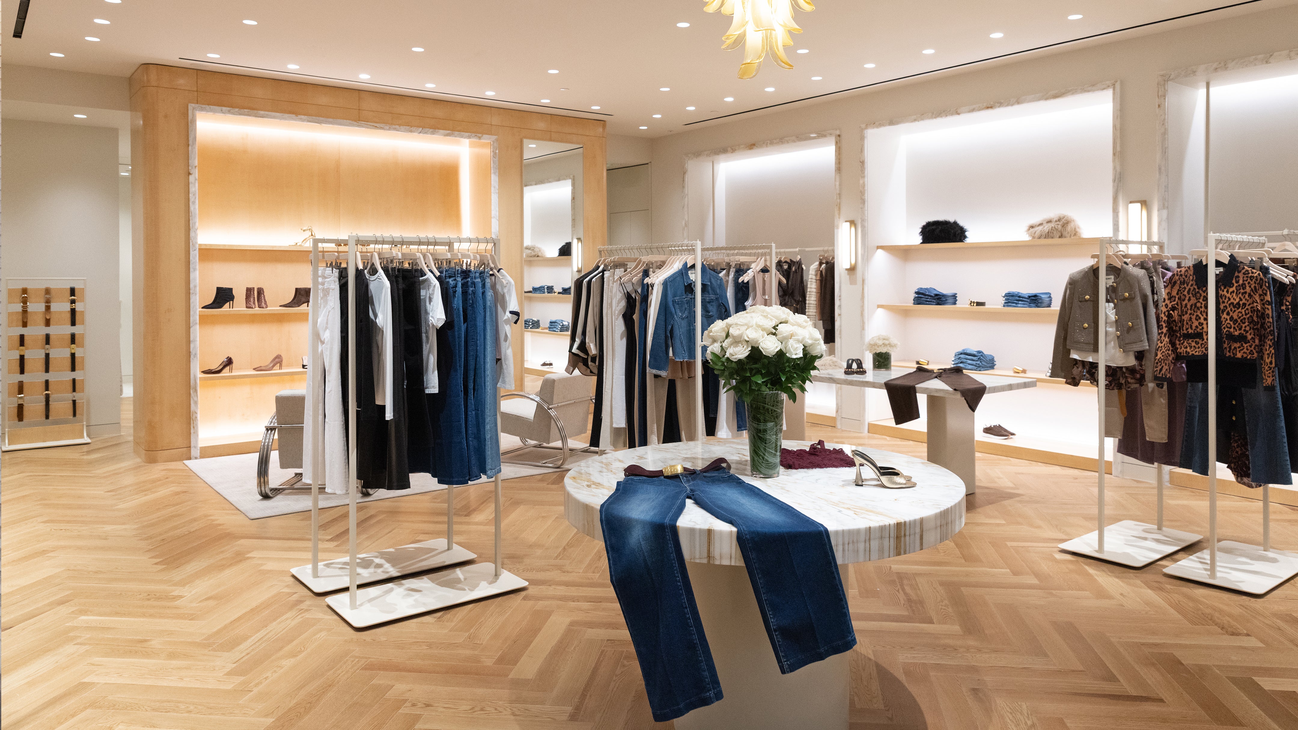 Clothing boutique interior featuring racks of apparel and a central display table with jeans and a vase of white roses.