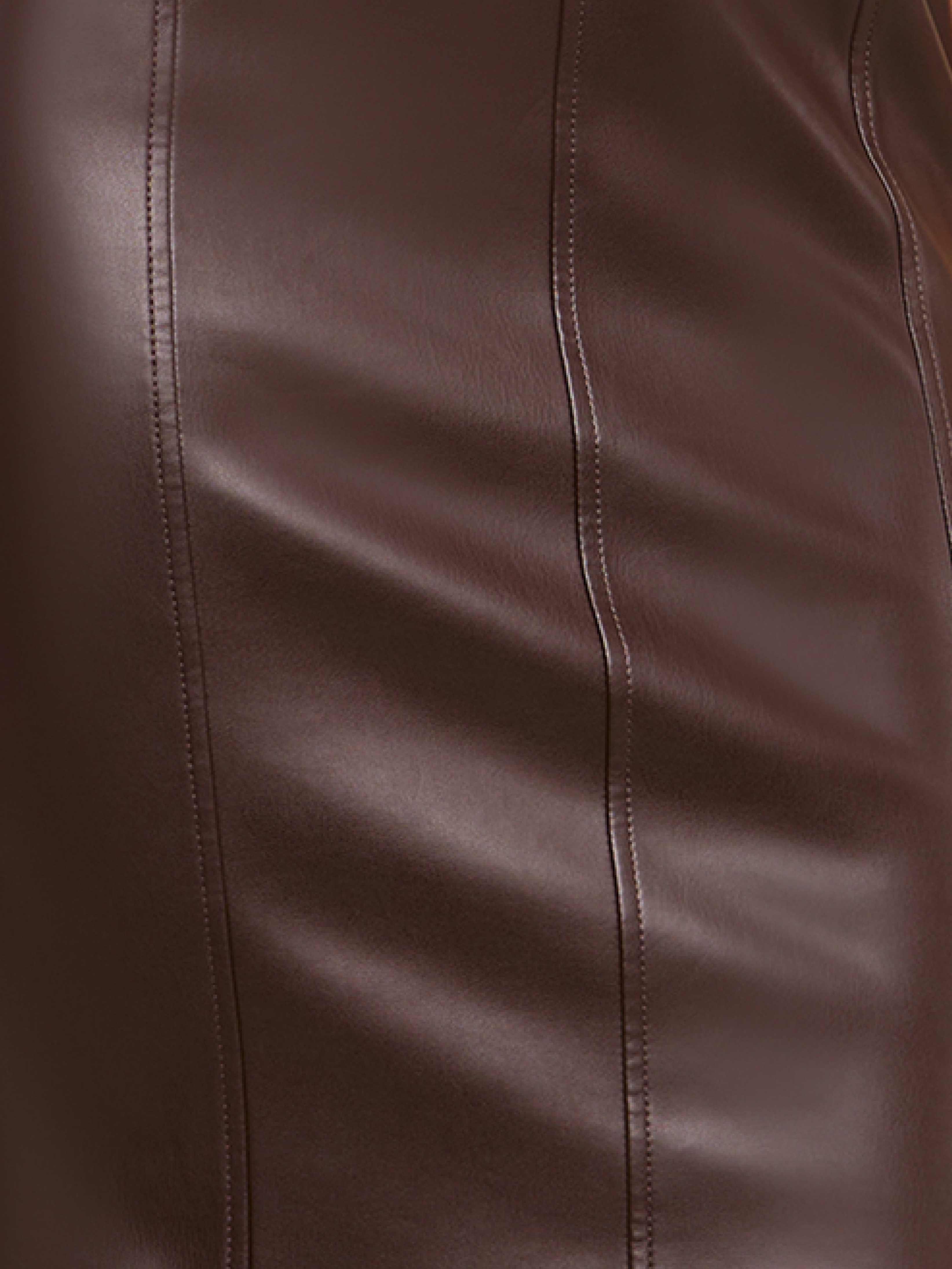 Close-up of a brown leather surface, showing vertical stitching and smooth texture with slight reflections.