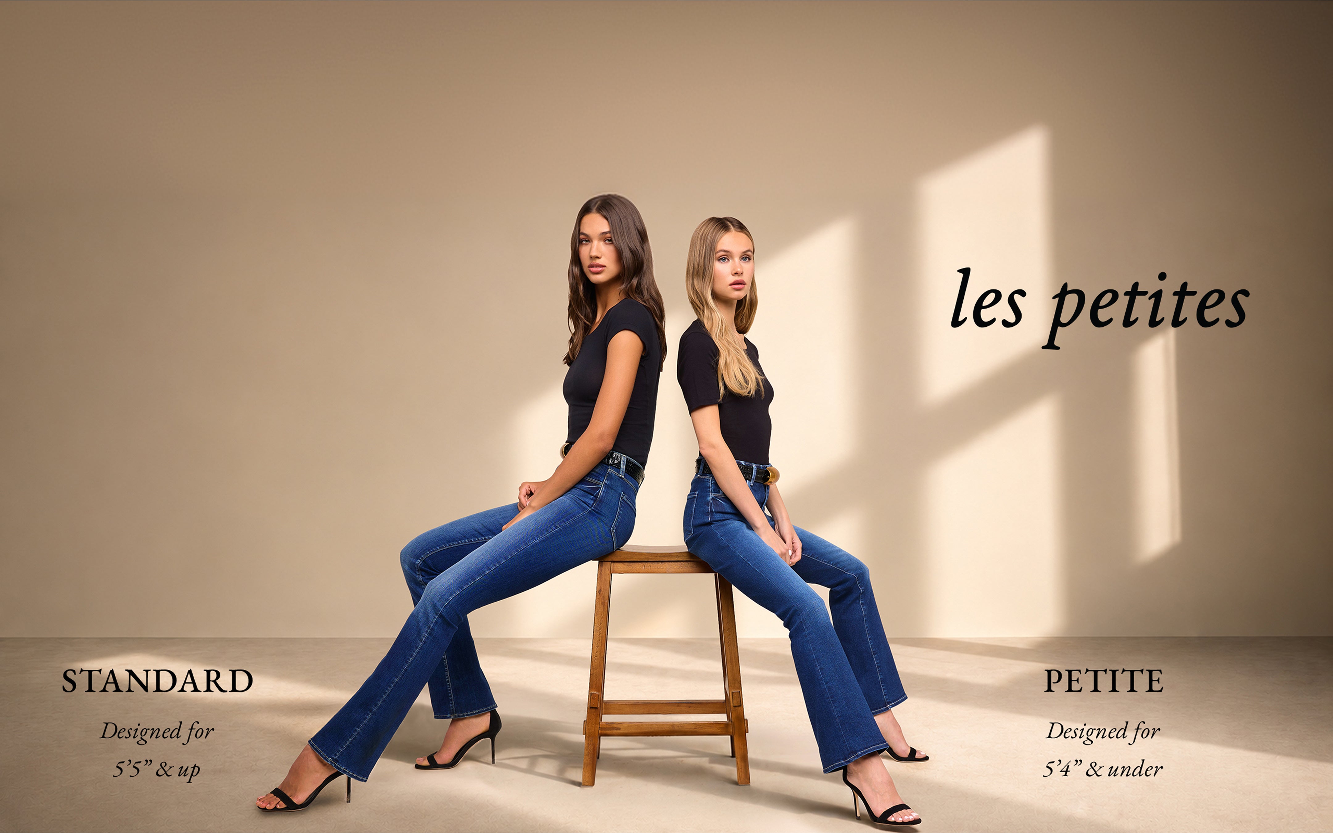 Two women in black tops and blue jeans sit back-to-back on stools. Text reads les petites, STANDARD Designed for 55  up, and PETITE Designed for 54  under. Neutral background with soft lighting.