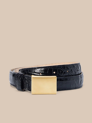 La cintura Amis, realizzata a mano in pelle italiana con disegno croc-embossed nero e fibbia rettangolare in oro, è presentata arrotolata su uno sfondo beige neutro.