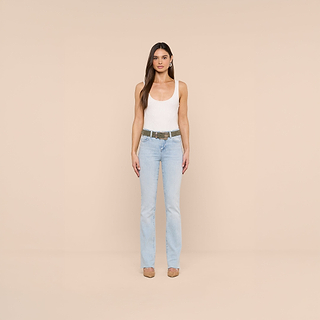 A woman stands against a beige background, wearing a white tank top, light blue jeans, taupe heels, and the Aya Suede Belt handcrafted in LA. She has long straight hair and a neutral expression, facing forward with her arms at her sides.