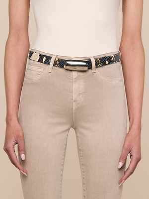 A person wears beige jeans, a white ribbed sleeveless top, and the Marlowe Leather Belt—python-embossed in black, blue, and beige with a silver-plated buckle. Their hands rest by their sides against a neutral background.