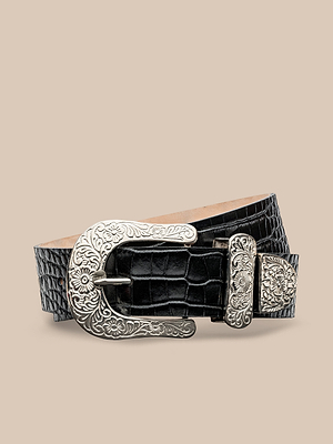 The Otera Leather Belt features black croc-embossed leather, handcrafted in LA, with a large ornate floral-engraved buckle and matching tip, shown against a neutral beige background.