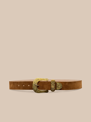 La cintura in pelle scamosciata Otera è caratterizzata da pelle scamosciata color cognac con fibbia in ottone inciso e punta dorata abbinata, realizzata a mano a Los Angeles e presentata su uno sfondo beige.