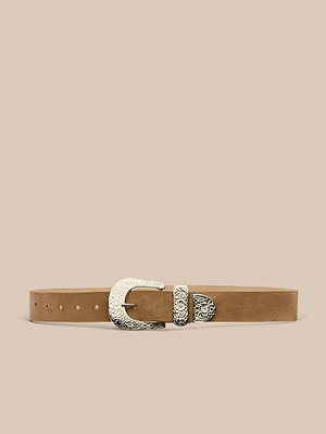 La ceinture en daim Otera est une ceinture en daim fauve fabriquée à la main à Los Angeles. Elle est dotée dune boucle, dun embout et dun passant en argent orné de motifs floraux gravés. Elle est présentée sur un fond beige.