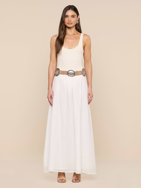 A woman stands against a beige background in a sleeveless cream top and long white skirt, styled with the Austin Suede Belt featuring large silver buckles. She has long hair and open-toed heels.