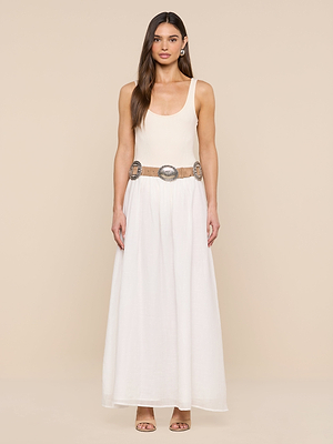 A woman stands against a beige background wearing a sleeveless cream top, long white skirt, and the Austin Suede Concho Belt with silver buckles. She has long straight hair and open-toe heels.