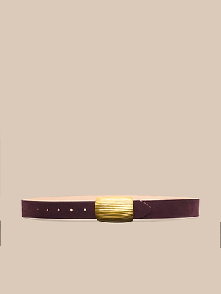 The Montell Suede Belt, handcrafted in Italy from rich burgundy suede and accented with a wide, ribbed gold buckle, is centered against a plain beige background.