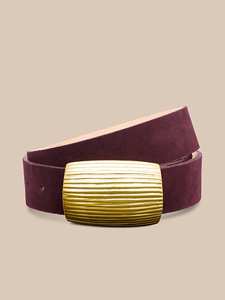 The Montell Suede Belt in burgundy, featuring a large rectangular gold-tone textured brass buckle, is coiled on a beige background.