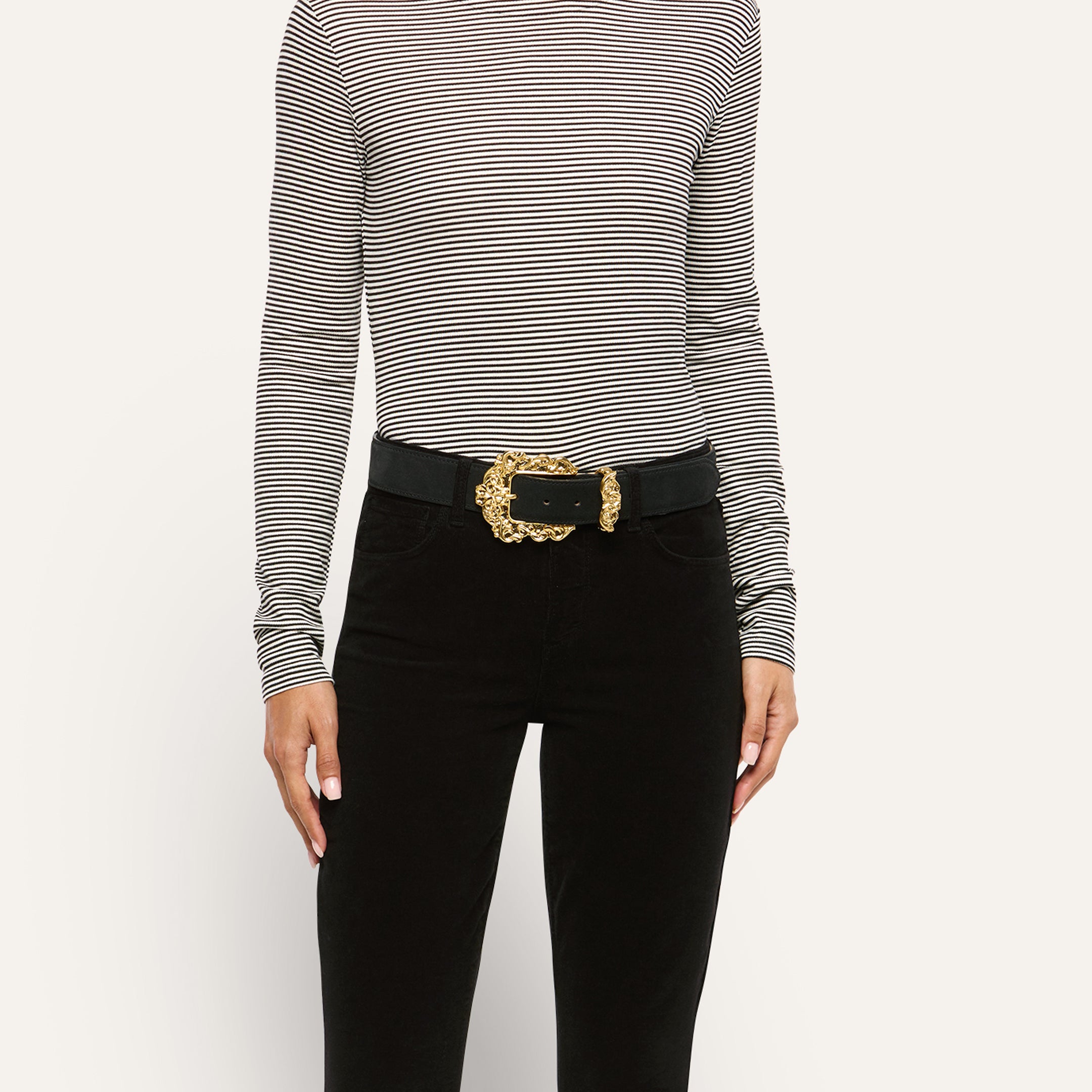 A person wearing an Italian calfsuede Caldera Suede Belt with an ornate gold-plated buckle over black pants and a black-and-white striped long-sleeve shirt.