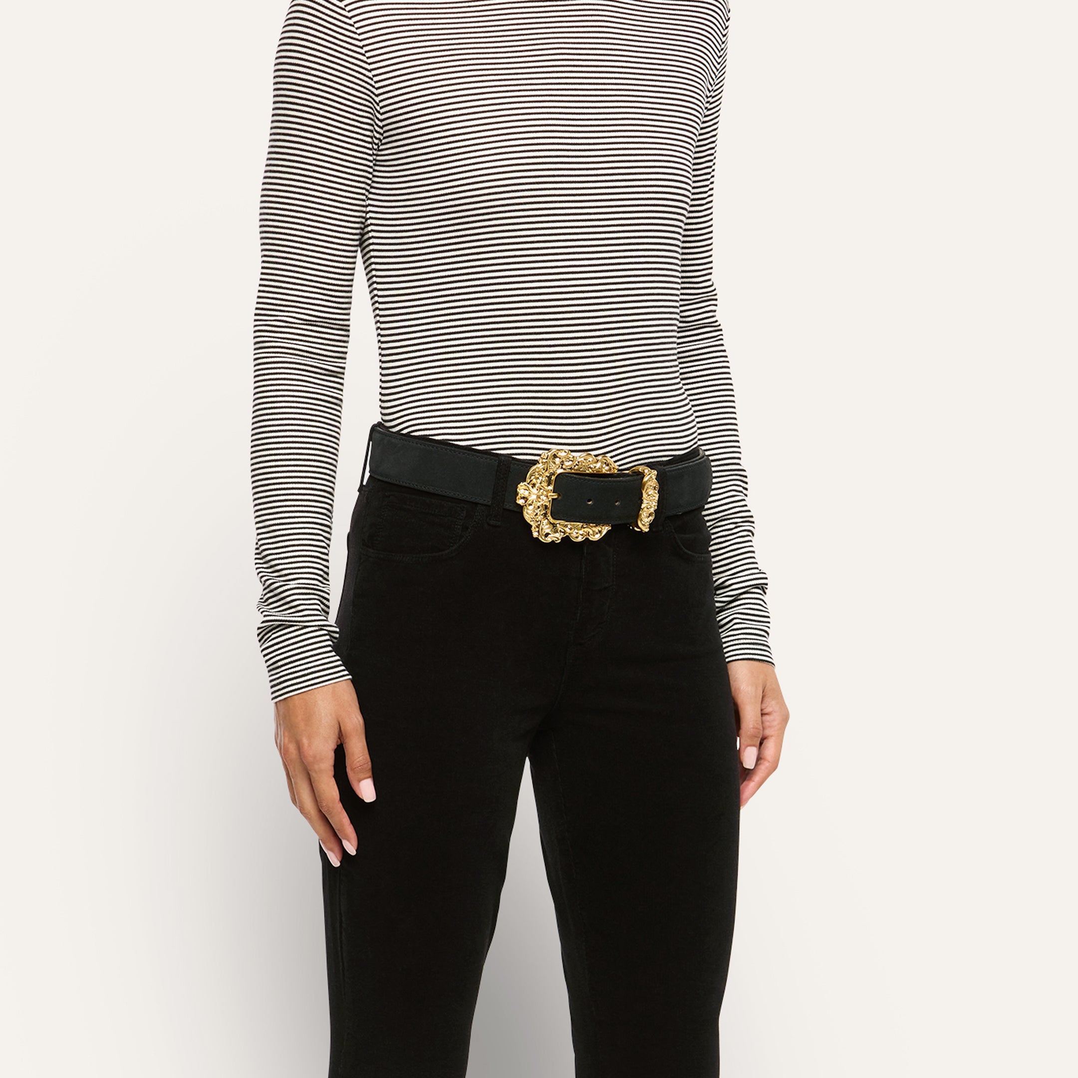 Caldera Suede Belt in black Italian calf suede with an ornate, gold-plated filigree buckle, worn over black pants and a striped long-sleeve shirt.