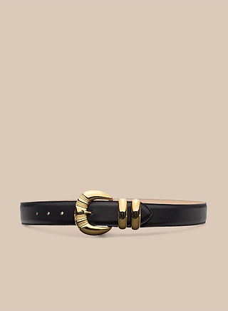 The Yarros Leather Belt, handcrafted in LA from black suede, features a large gold-plated circular buckle and two gold loops, and is elegantly displayed on a beige background.