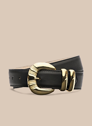 The Yarros Leather Belt, handcrafted in LA from black leather, features a large decorative gold-plated buckle and two matching gold belt loops, shown against a plain beige background.