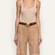 The Milou Belt, a handcrafted leopard print belt with a rectangular gold-tone metal buckle, worn over tan trousers and a beige ribbed tank top.