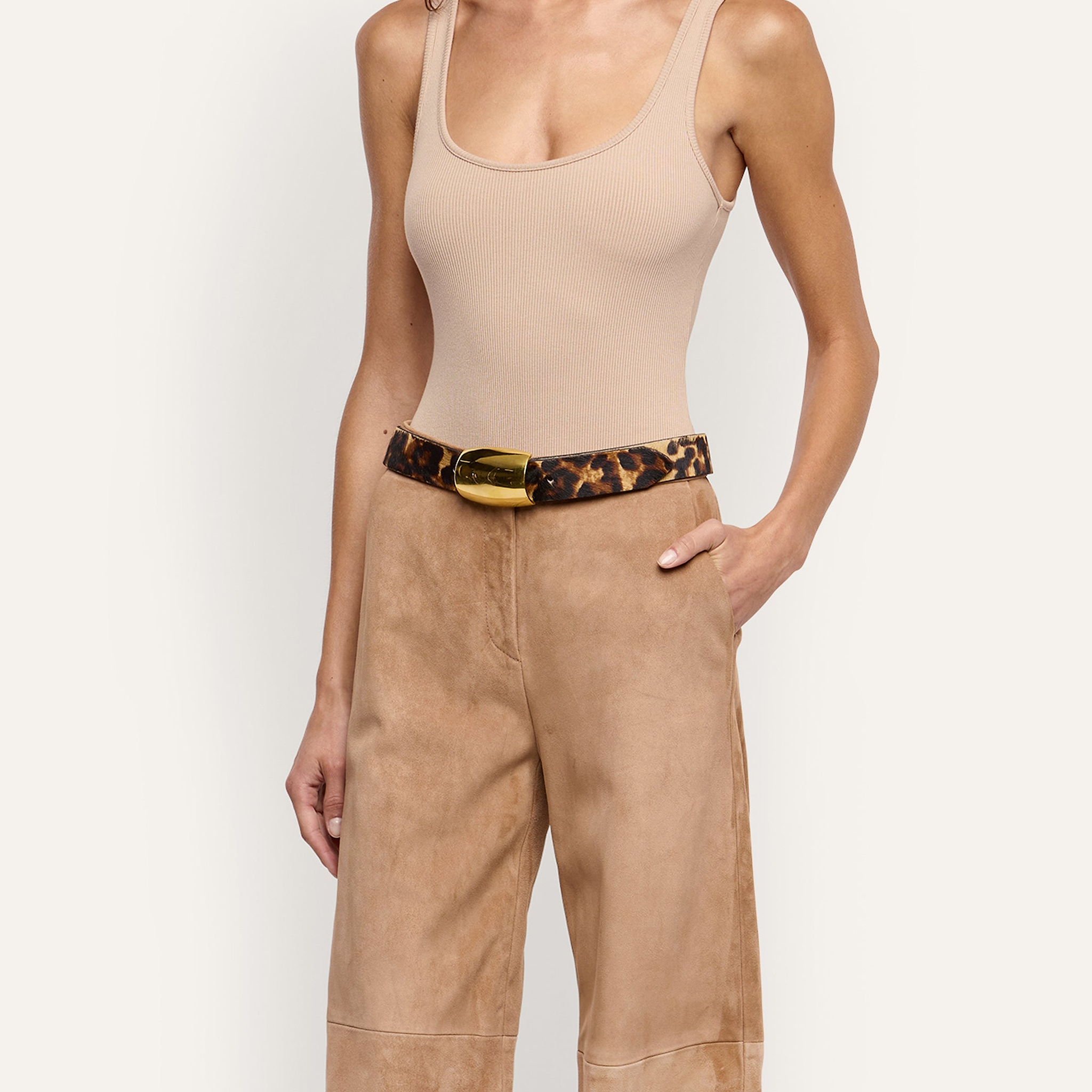 Milou Belt in leopard print Italian calf hair with a large, polished gold-tone rectangular buckle, worn with tan trousers and a beige tank top.