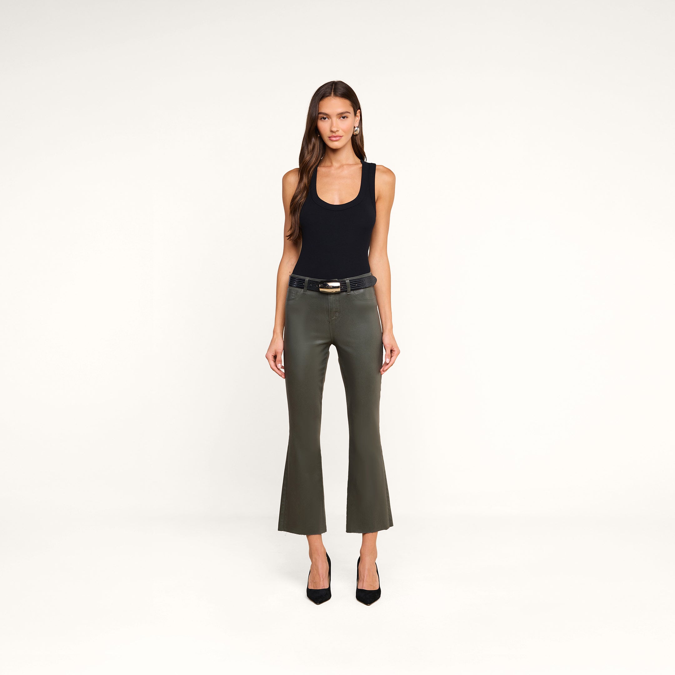 A woman stands facing forward against a plain white background, wearing a sleeveless black top, olive green flared pants, black heels, and accessorized with the Milou Belt.