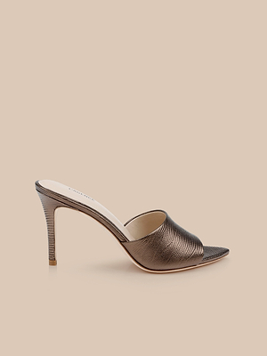 The Lolita Leather Open-Toe Mule features metallic bronze lizard-embossed leather, a textured finish, open toe, and a high stiletto heel, displayed on a beige background.
