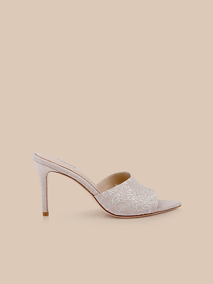 The Lolita Linen Open-Toe Mule is a single light beige shoe with floral lace on the upper and a chic linen stiletto heel, shown against a plain beige background.