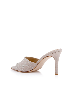 The Lolita Linen Open-Toe Mule features a high stiletto heel, light beige embroidered linen with a subtle lace pattern, and an open toe design, displayed against a white background.