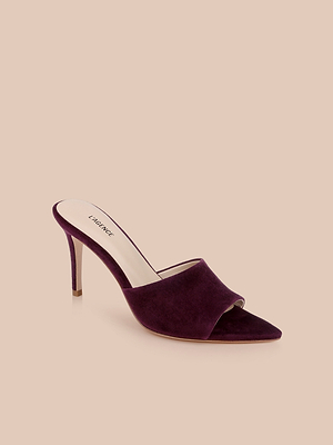 The Lolita Suede Open-Toe Mule in burgundy features a pointed toe, wide front strap, stiletto heel, and open back, shown against a neutral beige background.