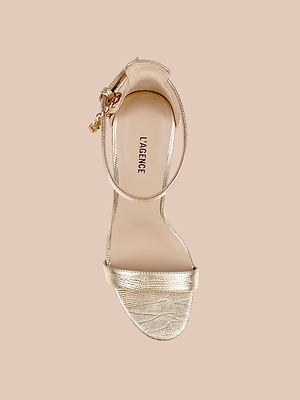 Il sandalo Gisele in pelle è un sandalo dorato con cinturino anteriore e fibbia testurizzata, mostrato dallalto su uno sfondo beige. Il sottopiede con letichetta LAGENCE lo rende perfetto come elegante scarpa da cerimonia.