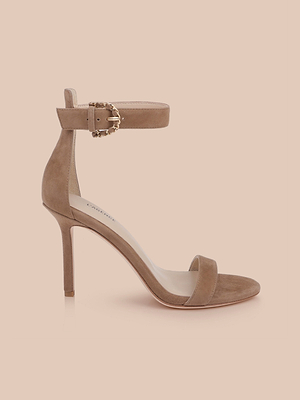 Il sandalo Gisele in pelle scamosciata è un tacco a spillo aperto in punta, color marrone caffè, con cinturino alla caviglia e fibbia dorata, su sfondo beige chiaro.