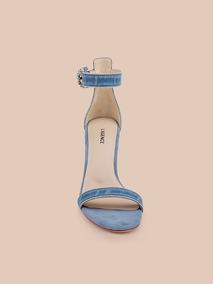 La sandalia vaquera Gisele, un zapato azul con correa en el tobillo, parte superior vaquera y puntera abierta, se muestra en posición vertical sobre un fondo beige liso.