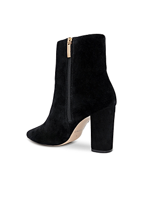 Theodora Block-Heel Bootie: A black suede bootie with a chunky block heel, pointed toe, side zipper with gold pull tab, and a light beige sole.