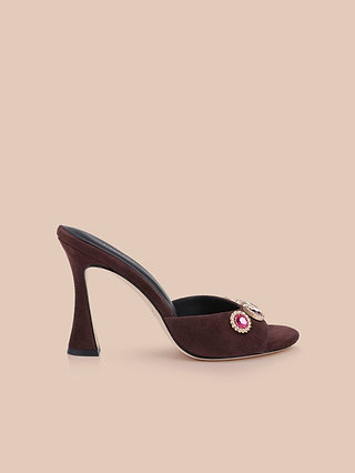 Introducing the Avery Suede Open-Toe Mule: this elegant mule showcases a flared heel and is crafted from rich mahogany brown suede. A decorative jeweled embellishment graces the front, while its burgundy hue stands out beautifully against a plain beige background.