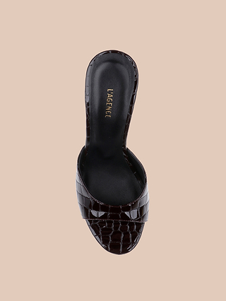 The Avery Leather Open-Toe Mule is a chic sandal in burgundy crocodile-embossed leather, showcasing an open toe and a black insole with “LAGENCE” printed in gold on the footbed, displayed against a beige background.