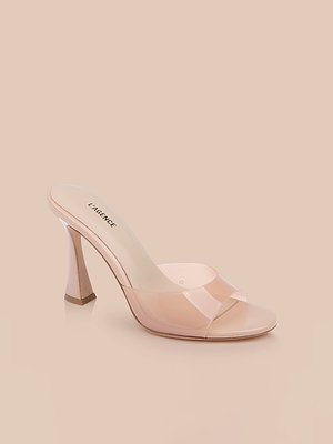 The Avery Open-Toe Mule, a light nude stiletto with a clear vamp, open toe, and square heel, is shown on a beige background.