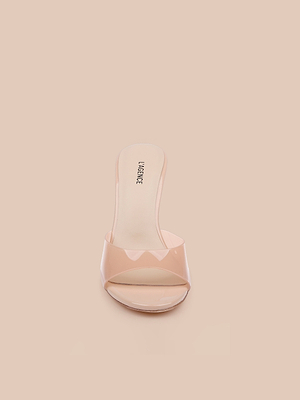 The Avery Open-Toe Mule is a light nude sculpted stiletto mule with a clear vamp and open toe, shown from the front on a matching beige background.