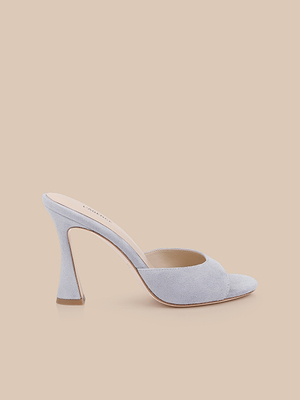 The Avery Suede Open-Toe Mule, in pale blue with a sculpted heel and light gray finish, is displayed on a beige background.