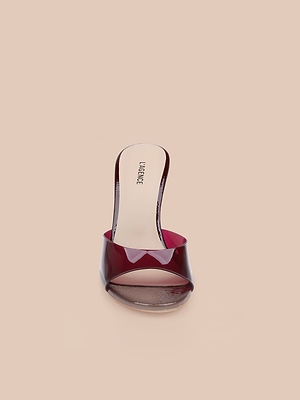 The Avery Open-Toe Mule is a chic sculpted stiletto featuring a transparent burgundy strap and beige insole, showcased front-facing against a light beige background.