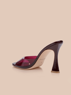 The Avery Open-Toe Mule, with a glossy curved stiletto heel, beige sole, and translucent burgundy upper, is displayed on a plain beige background.