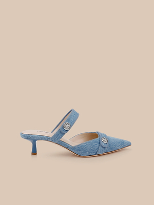 The Gilliane Denim Mule is a blue pointed-toe mule with two strapped accents, decorative round buttons, a low kitten heel, and a memory foam insole, shown on a beige background.